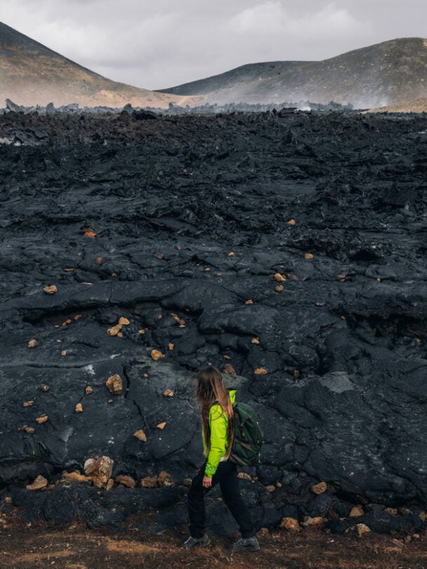 A woman hiking beside the firmed up lava close to the site of an erupting Iceland volcano.